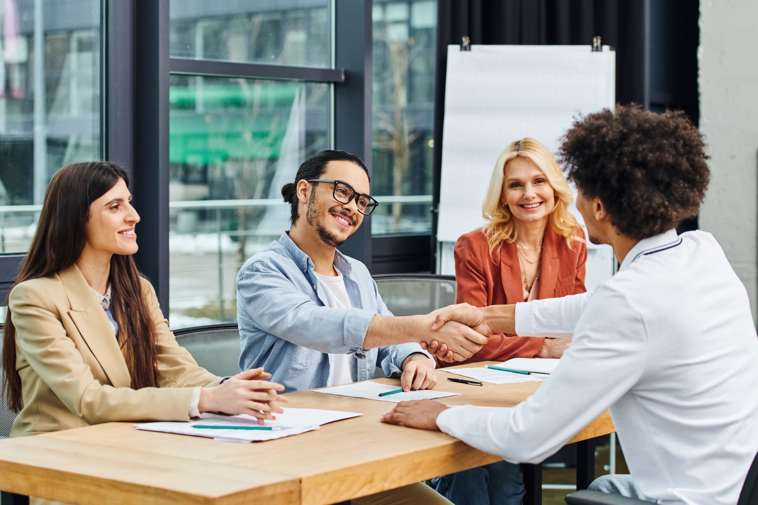 Deelnemer aan sollicitatietraining voert een succesvol sollicitatiegesprek en schudt handen met recruiter, met positieve reacties van gesprekspartners