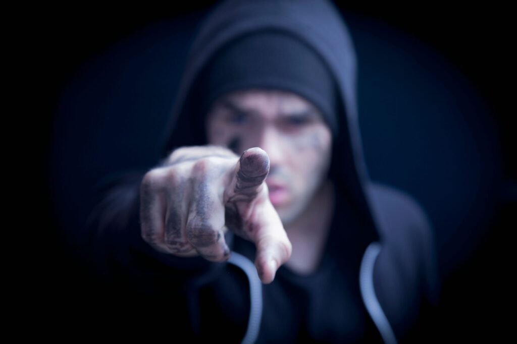 Man in hoodie wijst dreigend naar camera, verbeeldt agressief gedrag in risicovolle werksituatie.
