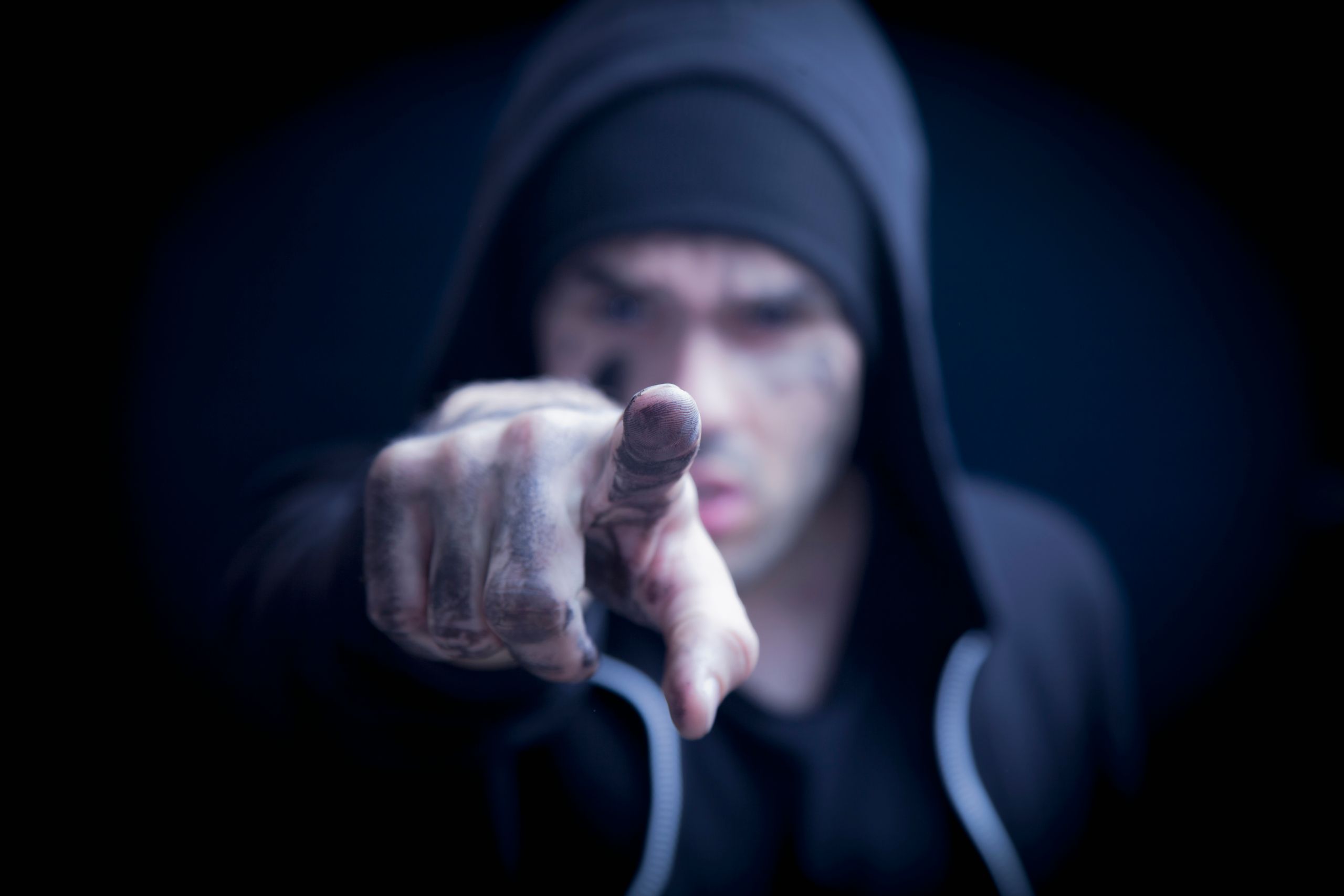 Man in hoodie wijst dreigend naar camera, verbeeldt agressief gedrag in risicovolle werksituatie.