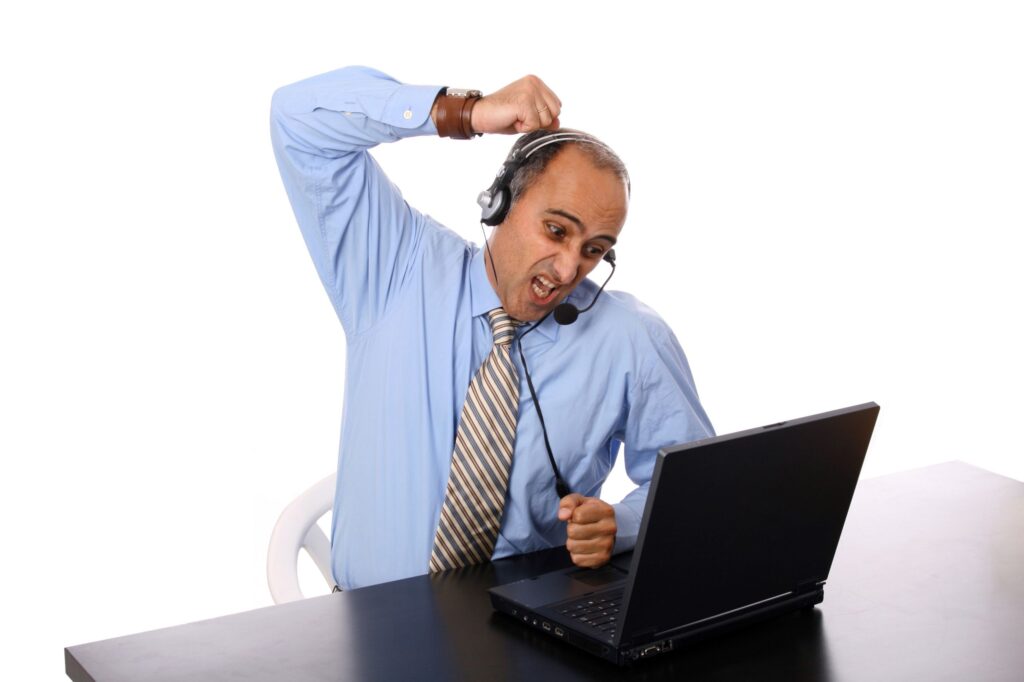 Man met headset reageert boos en gefrustreerd tijdens telefoongesprek via laptop, passend bij training over omgaan met telefonische agressie.